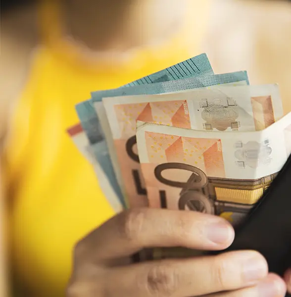 A person in a yellow top holds several Euro banknotes in their hand.